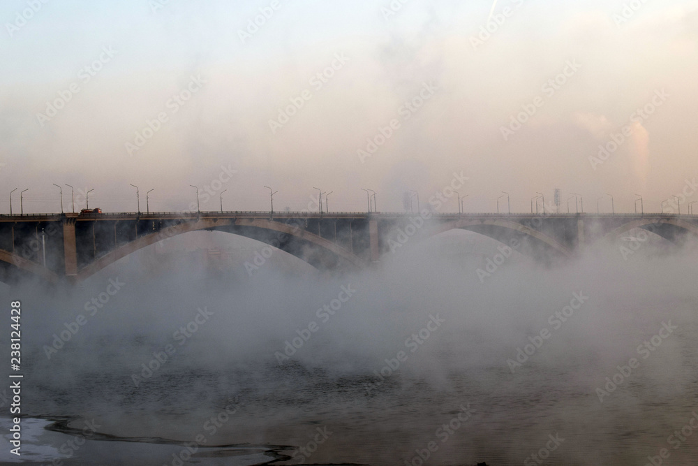 Communal bridge across the Yenisei river. Sights of Krasnoyarsk.  The mist over the water. Low air temperature.