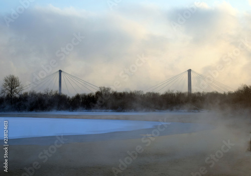 Pedestrian bridge in the city of Krasnoyarsk. Winter landscape. The ice on the river. The mist over the water. Low air temperature.