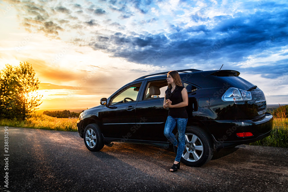 Girl near big black car and sunset over the road