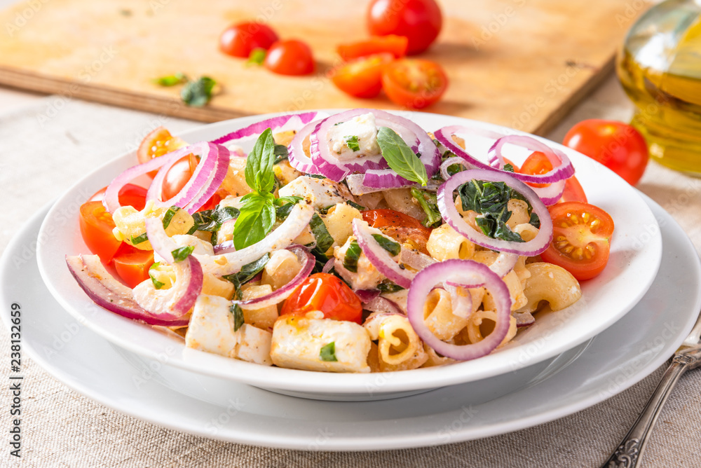 Warm pasta salad with cherry tomatoes, feta cheese and onions on a plate on the table Warm pasta salad with cherry tomatoes, feta cheese and onions on a plate on the table