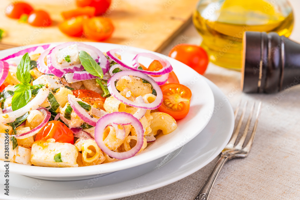 Warm pasta salad with cherry tomatoes, feta cheese and onions on a plate on the table Warm pasta salad with cherry tomatoes, feta cheese and onions on a plate on the table