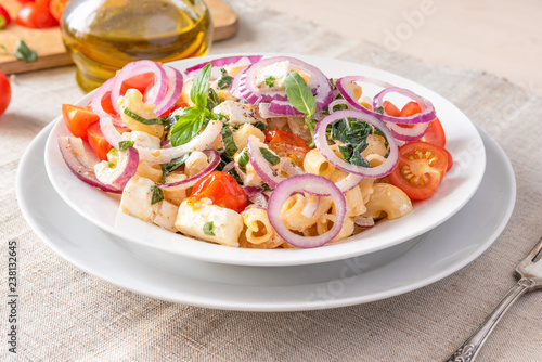 Warm pasta salad with cherry tomatoes, feta cheese and onions on a plate on the table