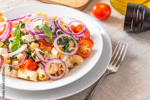 Warm pasta salad with cherry tomatoes, feta cheese and onions on a plate on the table