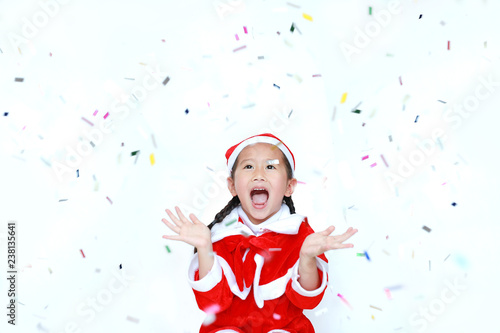 Happy child girl in Santa costume dress with colorful confetti on white background. Merry Christmas and Happy New Year Concept.