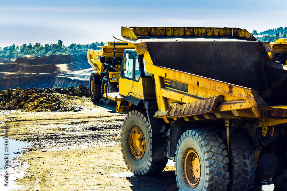Fototapeta premium Yellow truck from behind and another in front with the mines in the background