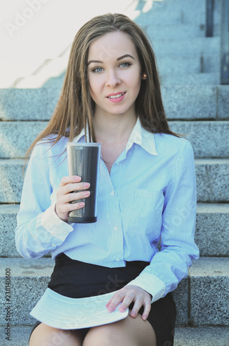 Beautiful young girl student, sat down on the steps during the break, drinking hot tea