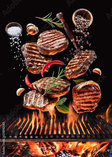 Grilled beef steaks with vegetables and spices fly over the glowing grill barbecue fire.