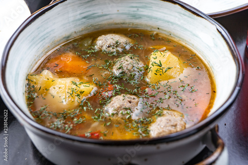 Soup with meat meatballs, potatoes and vegetables. in a white plate on a black background