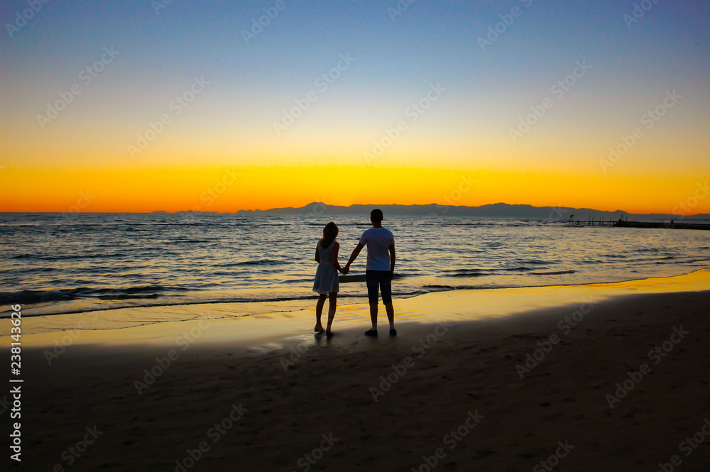 Romantic couple holding hands and enjoying the sunrise on a warm summer day.