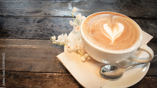 Coffee cup and tiny white flower on wood table.