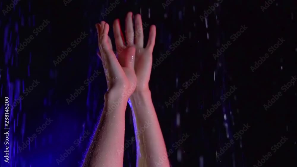 young woman is standing under rain in blue neon light, stretching hands up young woman is standing under rain in blue neon light, stretching hands up