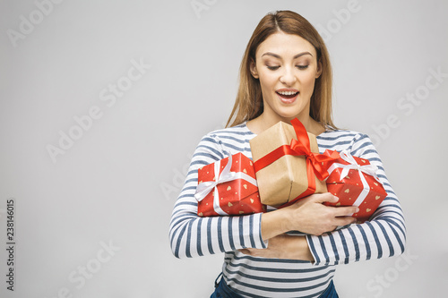 Nice surprise! Happy brunette woman holding big pile of gifts. Isolated over white background.