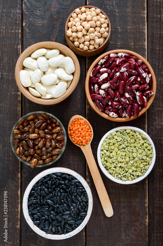 Healthy food, dieting, nutrition concept, vegan protein source. Assortment of colorful raw legumes: red lentils, green peas, beans, chickpeas in bowls, on a wooden table. Top view, flat lay background