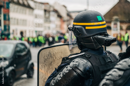 Photography Rear view of police officer wearing helmet and shield securing the zone in frong of the Yellow vests movement gilets jaunes protesters on Quai des Bateliers street