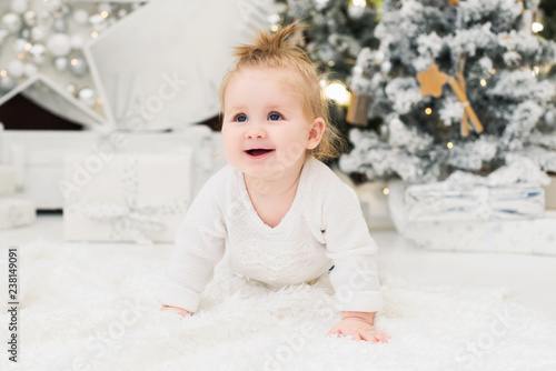 Baby girl on a background of Christmas trees, lights and gift boxes