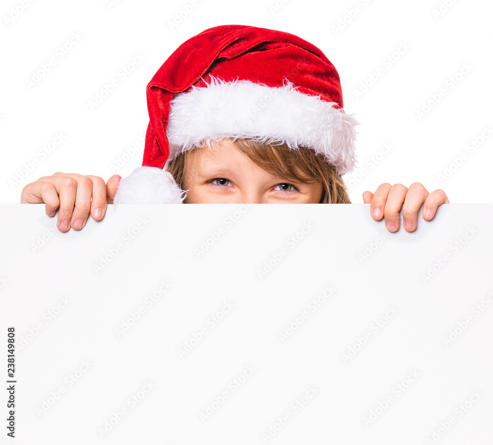 Little girl wearing Santa Claus hat, posing behind white panel isolated on white background. Kid holding empty Christmas billboard. Child peeping behind blank holidays board. Little girl wearing Santa Claus hat, posing behind white panel isolated on white background. Kid holding empty Christmas billboard. Child peeping behind blank holidays board.