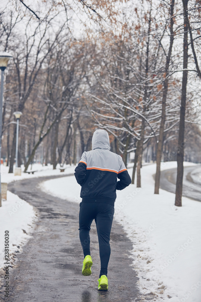 Man jogging in a cold winter snowy day outdoors.