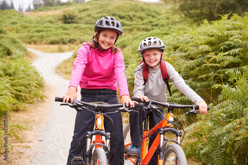 Two children sitting on their mountain bikes on a country path laughing, front view