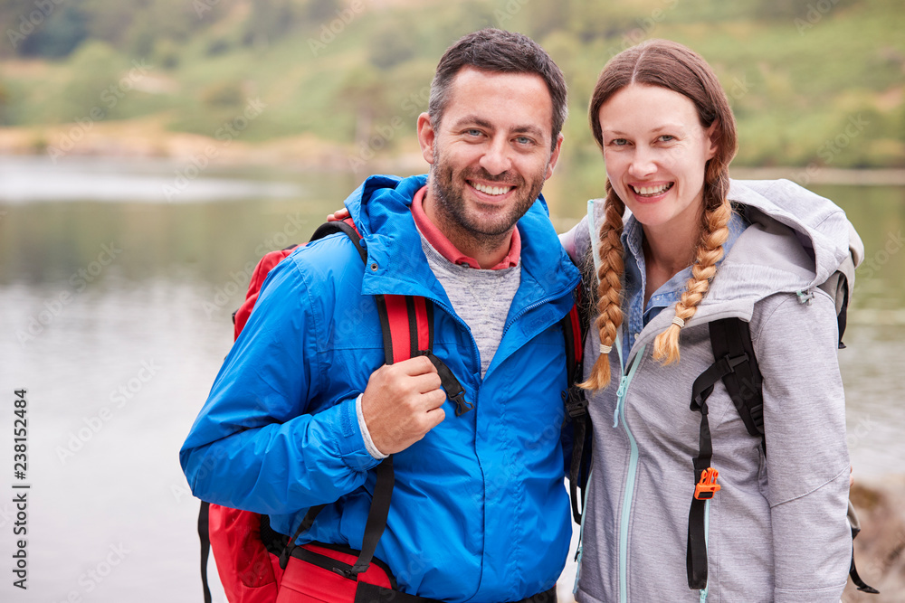 Young adult couple on a camping trip standing near a lake looking to camera, close up, Lake District, UK