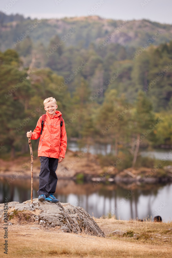 A boy standing on a rock by a lake holding a stick, smiling to camera, Lake District, UK, vertical A boy standing on a rock by a lake holding a stick, smiling to camera, Lake District, UK, vertical