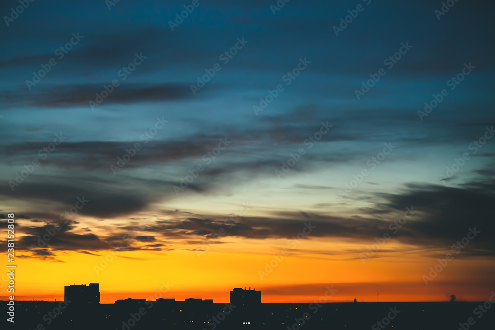Cityscape with wonderful varicolored vivid dawn. Amazing dramatic blue cloudy sky above dark silhouettes of city buildings. Atmospheric background of orange sunrise in overcast weather. Copy space. Cityscape with wonderful varicolored vivid dawn. Amazing dramatic blue cloudy sky above dark silhouettes of city buildings. Atmospheric background of orange sunrise in overcast weather. Copy space.