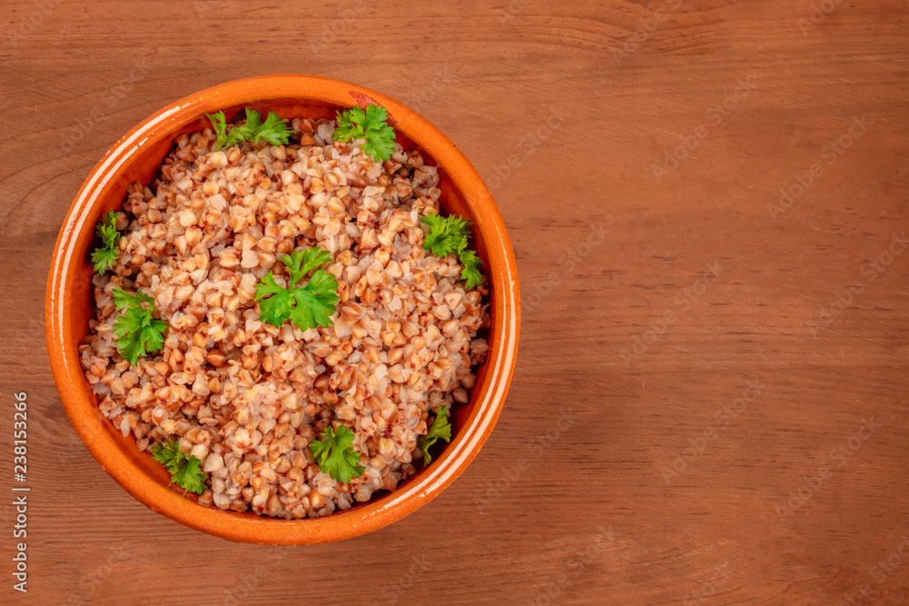 An overhead photo of cooked buckwheat in an earthenware bowl, garnished with fresh parsley leaves, on a dark rustic wooden background with a place for text An overhead photo of cooked buckwheat in an earthenware bowl, garnished with fresh parsley leaves, on a dark rustic wooden background with a place for text