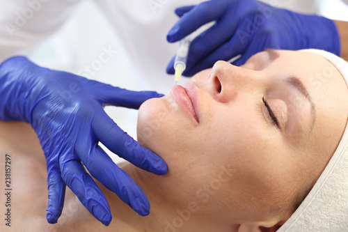 Powiększanie ust. Pacjentka w klinice kosmetycznej, kosmetyczka wykonuje zabieg ostrzykiwania.