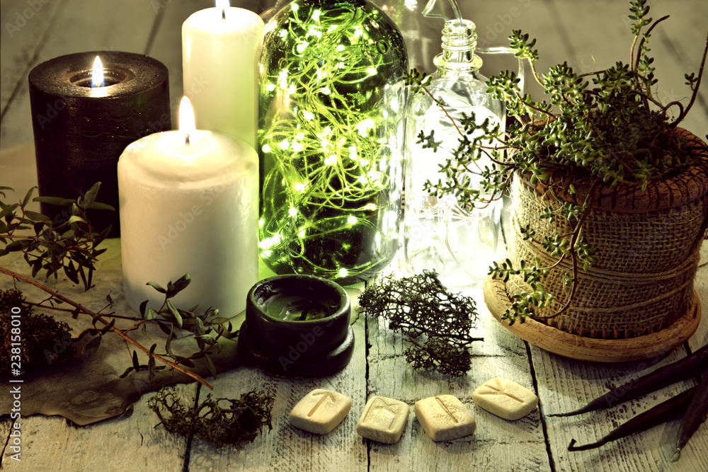 Still life with ancient runes, black and white candles, shining bottles