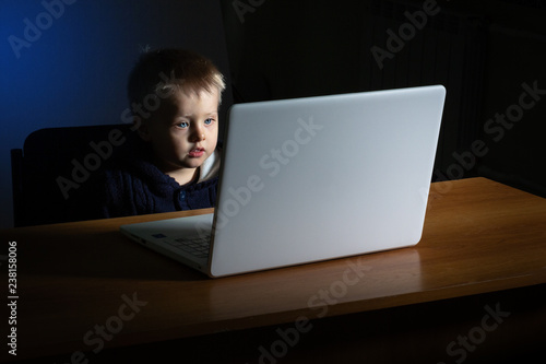 A little boy uses a laptop in the dark.