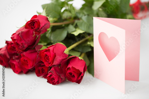 love, valentines day and holidays concept - close up of red roses bunch and greeting card with heart