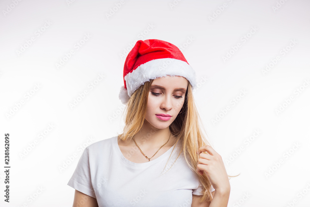 Sad Santa girl on white background looking down. Beautiful blonde woman wearing red Santa hat and t-shirt Sad Santa girl on white background looking down. Beautiful blonde woman wearing red Santa hat and t-shirt