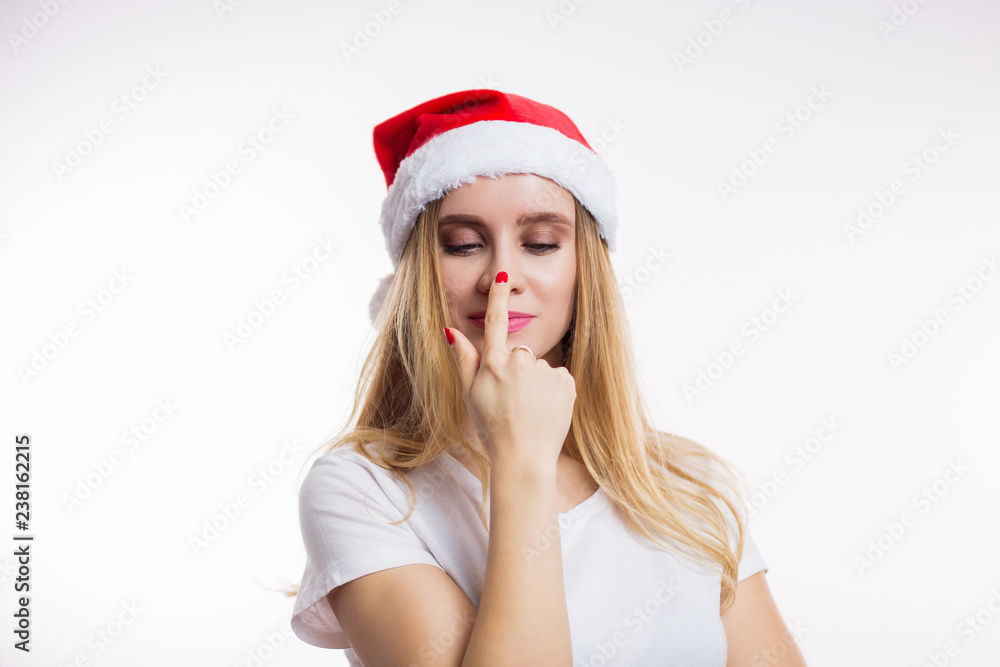 Beautiful funny blonde woman wearing red Santa hat smiling and finger pointing at her nose on white background Beautiful funny blonde woman wearing red Santa hat smiling and finger pointing at her nose on white background