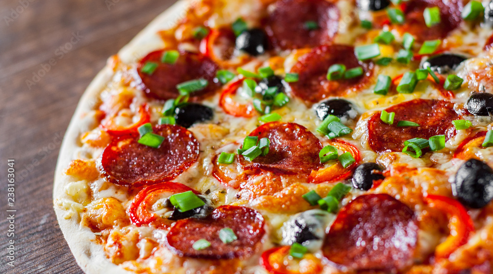 Pizza with Mozzarella cheese, pepperoni, tomato, pepper, olive, salami. Italian pizza on wooden table background Pizza with Mozzarella cheese, pepperoni, tomato, pepper, olive, salami. Italian pizza on wooden table background