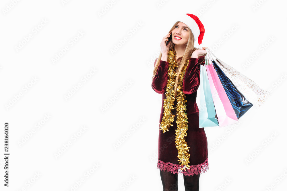 Beautiful woman in santa hat, with christmas bags in hand, talking on smartphone.