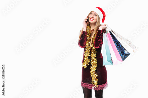 Beautiful woman in santa hat  with christmas bags in hand  talking on smartphone.