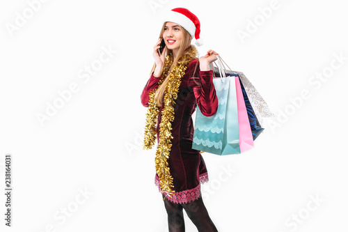 Beautiful woman in santa hat, with christmas bags in hand, talking on smartphone.
