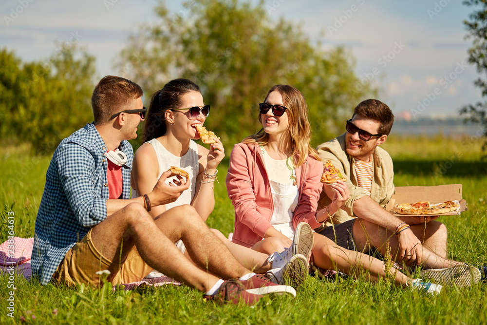 Fototapeta premium friendship, leisure and food concept - group of smiling friends eating pizza at picnic in summer park