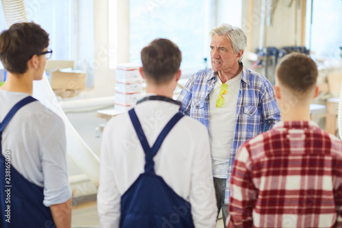 Angry displeased mature carpenter foreman with gray hair standing in front of young employees and yelling at them while dressing down them for poor performance