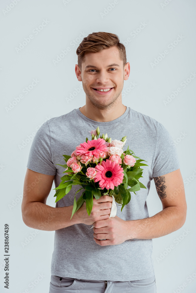 smiling man looking at camera and holding pink flower bouquet isolated on grey smiling man looking at camera and holding pink flower bouquet isolated on grey