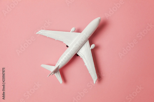 Simply flat lay design miniature toy model plane on pink pastel colorful paper trendy background. Travel by plane vacation summer weekend sea adventure trip journey ticket tour concept