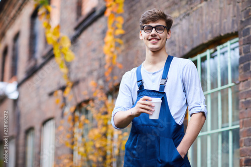 Foto Smiling confident handsome factory worker in blue overall and glasses holding ha