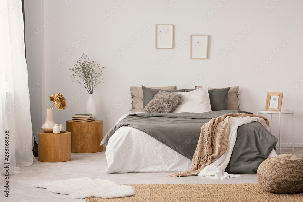 Flowers on wooden stool and pouf in white bedroom interior with posters above bed. Real photo - obrazy, fototapety, plakaty 