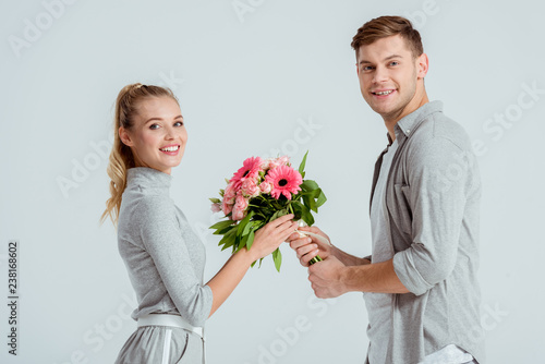 handsome man giving flower bouquet to beautiful smiling woman isolated on grey © LIGHTFIELD STUDIOS