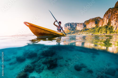 Young woman paddles kayak in a tropical sea. Splitted shot with underwater stones view