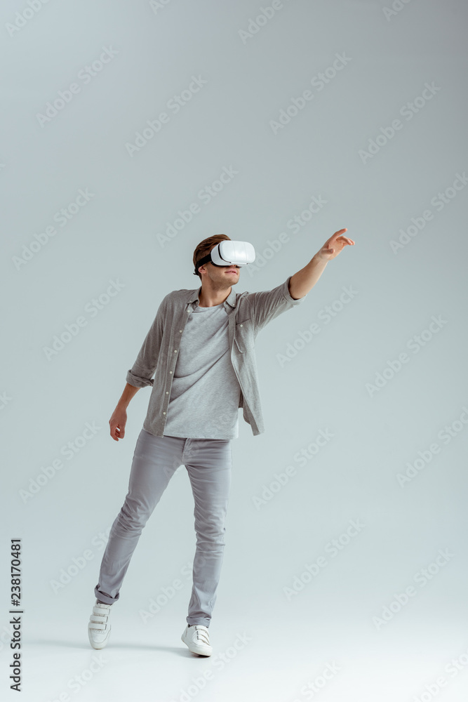 man in grey clothing gesturing while wearing virtual reality headset on grey background man in grey clothing gesturing while wearing virtual reality headset on grey background