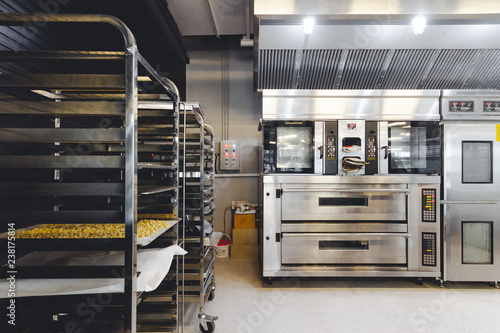 Modern pastry kitchen decorated in black, white and steel with baking machine, oven, conveyor, production line, mixer and cooling plant.