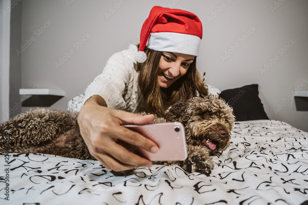 .Young and cheerful woman playing with her nice spanish water dog on Christmas morning, taking some pictures with her smart phone. Both with christmas costume. Lifestyle. .Young and cheerful woman playing with her nice spanish water dog on Christmas morning, taking some pictures with her smart phone. Both with christmas costume. Lifestyle.