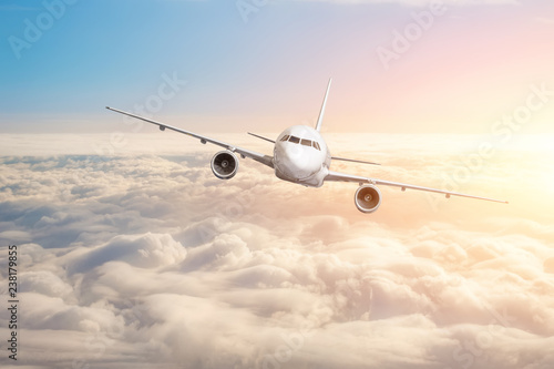 Passenger aircraft flying above the clouds horizon sky with bright sunset colors