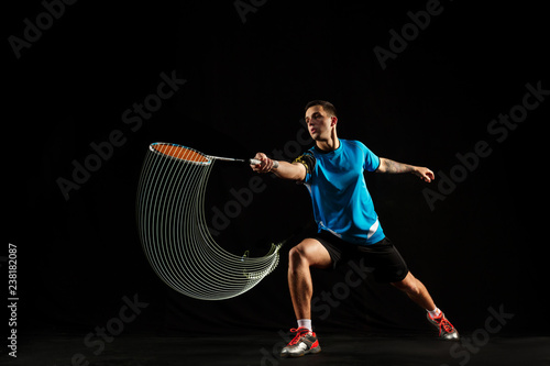 Young man playing badminton over black studio background. Fit male athlete isolated on dark with led light trail . badminton player in action, motion, movement. attack and defense concept © master1305