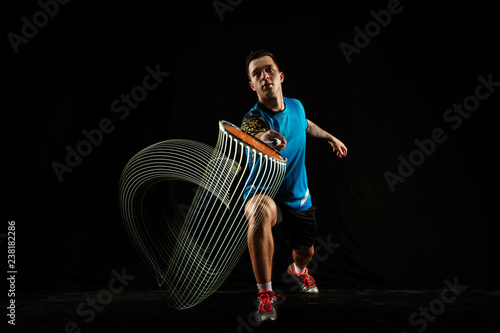 Young man playing badminton over black studio background. Fit male athlete isolated on dark with led light trail . badminton player in action, motion, movement. attack and defense concept